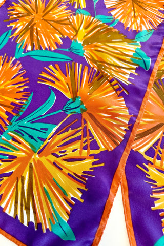 Long, rectangular vintage silk scarf by Vera, with royal purple background and bold orange and green dandelion print. 