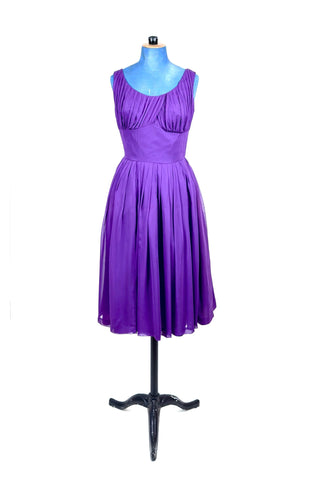 Show-stopping vintage 1950s party dress in bright purple chiffon. The voluminous skirt is pleated at the waist, echoing the gathered draped bust. The wide scoop neckline highlights your décolletage. Lined in purple chiffon, with a reinforced cotton inset waist lining for extra structure. Closes in the back with a metal zipper.