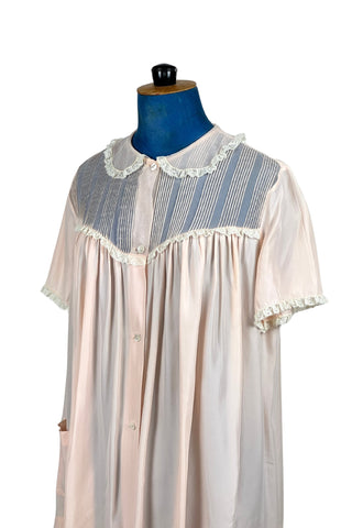 Charming vintage 1950s bed jacket pajama top in silky pink acetate & rayon by Barbizon “Lazy Lizzie”. Beautifully constructed with an inset yoke panel of sheer acetate with delicate pintucks, a Peter Pan collar edged with gathered lace trim, and short sleeves also trimmed in lace. Closes with four mother-of-pearl buttons. 