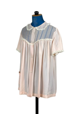 Charming vintage 1950s bed jacket pajama top in silky pink acetate & rayon by Barbizon “Lazy Lizzie”. Beautifully constructed with an inset yoke panel of sheer acetate with delicate pintucks, a Peter Pan collar edged with gathered lace trim, and short sleeves also trimmed in lace. Closes with four mother-of-pearl buttons. 