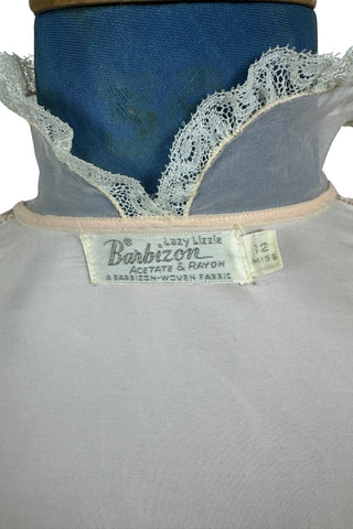 Charming vintage 1950s bed jacket pajama top in silky pink acetate & rayon by Barbizon “Lazy Lizzie”. Beautifully constructed with an inset yoke panel of sheer acetate with delicate pintucks, a Peter Pan collar edged with gathered lace trim, and short sleeves also trimmed in lace. Closes with four mother-of-pearl buttons. 