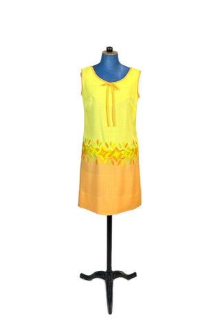 Darling vintage 1960s shift dress with orange bow tie and bold floral embroidery. The yellow bodice and orange skirt meet at the hip with a large band of stylized floral embroidery in shades of yellow, orange, and green. The neckline and arms are finished with matching orange binding. 