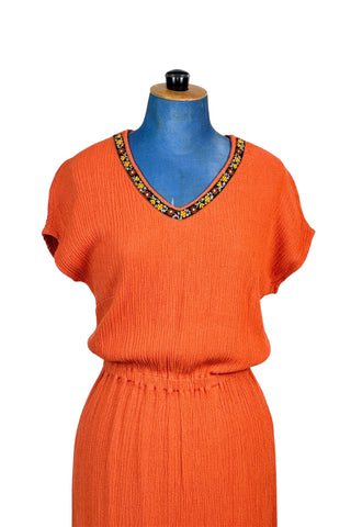 Vintage 1970s orange maxi dress with V-neck  in textured rayon crepe. There are high slits on both sides of the skirt. The neckline and side slits are adorned with floral embroidered trim. The waist is elasticized. The dress is unlined. 