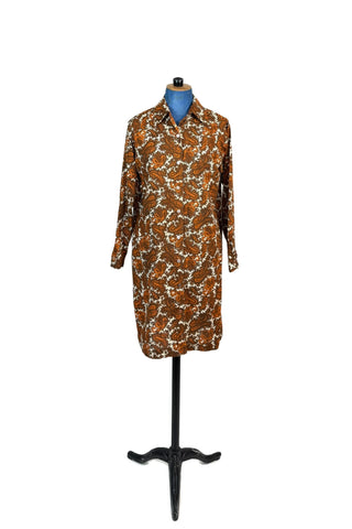 Vintage 1970s cotton shirt dress in brown and orange paisley. Closes with ten buttons down the front. Features a pointed collar, long sleeves with buttoned cuffs, and a simple yet chic A-line shape. The collar has the option of being buttoned fully closed or leaving one button open for a more relaxed look.