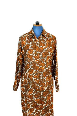 Vintage 1970s cotton shirt dress in brown and orange paisley. Closes with ten buttons down the front. Features a pointed collar, long sleeves with buttoned cuffs, and a simple yet chic A-line shape. The collar has the option of being buttoned fully closed or leaving one button open for a more relaxed look.