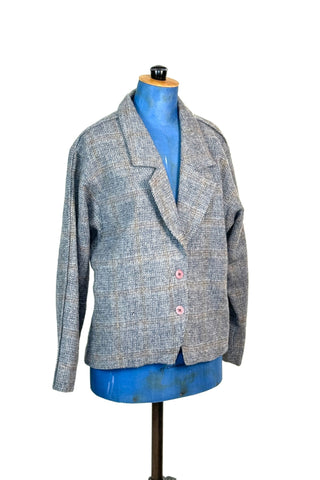 Vintage late 1970s, early 1980s grey wool blazer jacket in 100% pure new wool. The windowpane tweed weave has a subtle pattern in shades of blue, yellow, and gold. Closes with two salmon pink buttons. Fully lined in pink acetate. 