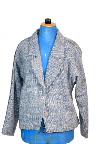 Vintage late 1970s, early 1980s grey wool blazer jacket in 100% pure new wool. The windowpane tweed weave has a subtle pattern in shades of blue, yellow, and gold. Closes with two salmon pink buttons. Fully lined in pink acetate. 