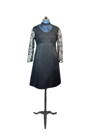 This stunning vintage 1960s cocktail dress combines a chic black A-line shift in smooth, heavyweight nylon, with delicately embroidered sheer sleeves, high neck, and bodice. Iridescent black thread adds dimension and depth to the swirling, botanical-inspired embroidery. Closes in the back with a cotton twill zipper.