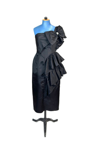 Incredible vintage 1980s cocktail dress in black rayon with tiered ruffles at the shoulder and down the left hip. A giant bow is draped at the shoulder, finished with a sparkling band of rhinestones. The 1940s-inspired draping and fit of this dress are impeccable, with a nipped waist and figure-hugging bodice and skirt. Closes with a zipper and hook-and-eye closure at the back. 