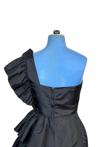 Incredible vintage 1980s cocktail dress in black rayon with tiered ruffles at the shoulder and down the left hip. A giant bow is draped at the shoulder, finished with a sparkling band of rhinestones. The 1940s-inspired draping and fit of this dress are impeccable, with a nipped waist and figure-hugging bodice and skirt. Closes with a zipper and hook-and-eye closure at the back. 