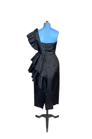 Incredible vintage 1980s cocktail dress in black rayon with tiered ruffles at the shoulder and down the left hip. A giant bow is draped at the shoulder, finished with a sparkling band of rhinestones. The 1940s-inspired draping and fit of this dress are impeccable, with a nipped waist and figure-hugging bodice and skirt. Closes with a zipper and hook-and-eye closure at the back. 