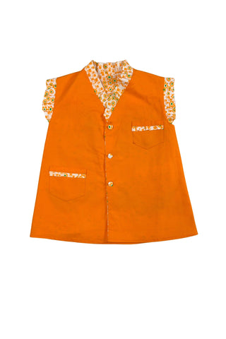 Bright tangerine orange reversible vintage 1960s girls’ vest with orange and green floral print. Each reversible side has pockets trimmed in the reverse-side fabric. The neckline and sleeve holes are trimmed with self-fabric ruffles.
