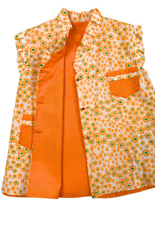 Bright tangerine orange reversible vintage 1960s girls’ vest with orange and green floral print. Each reversible side has pockets trimmed in the reverse-side fabric. The neckline and sleeve holes are trimmed with self-fabric ruffles.