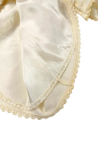 This darling vintage 1960s cape and dress set is embroidered with pink cherry blossoms and pink, blue and yellow tulips. The cape has a detachable hood which attaches with buttons at the back and sides of the cape’s round Peter Pan collar. The collar and hem of the cape are trimmed with scalloped crocheted lace. The cape has a double-breasted front closure with white and silver tone square buttons. There are arm holes in the middle of the front seams.