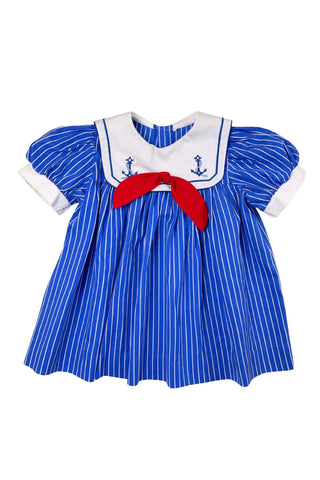 Adorable vintage 1980s toddler sailor dress with separate blue and white striped under-dress and white bib-collar pinafore apron which closes in the back with blue and white buttons. The sailor collar of the dress is embroidered with two anchors and finished with a bright red bow tie, while the pinafore has a matching blue stripe around the hem. The dress closes in the back with two buttons.
