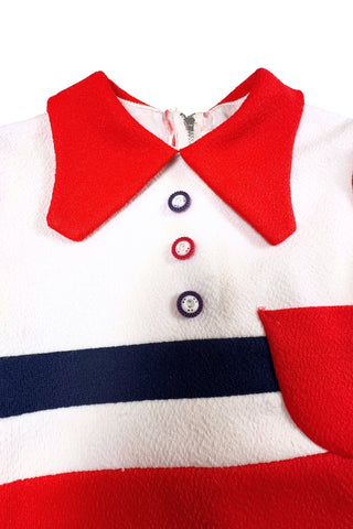 Vintage 1970s children’s dress with red skirt and sleeves, white bodice, and red pointed collar and matching pocket. The bodice and skirt feature contrasting navy blue stripes vertically and horizontally. Three decorative buttons at the neck finish this perfect late-mod look. The dress closes with a metal zipper in the back, and is fully lined in dove grey rayon.