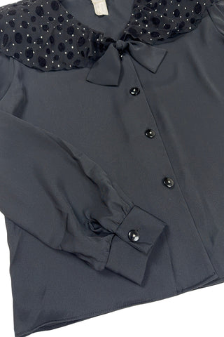 Vintage 1980s sheer black blouse with a chiffon collar featuring velvet polkadots and dots of silver sparkles. The blouse closes with four black buttons with rhinestone centres. The cuffs have matching button closures. The blouse comes with a separate tie piece that can be tied around the neck, or left off for a different look.