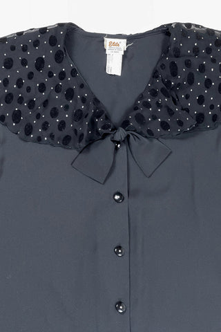 Vintage 1980s sheer black blouse with a chiffon collar featuring velvet polkadots and dots of silver sparkles. The blouse closes with four black buttons with rhinestone centres. The cuffs have matching button closures. The blouse comes with a separate tie piece that can be tied around the neck, or left off for a different look.
