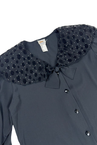 Vintage 1980s sheer black blouse with a chiffon collar featuring velvet polkadots and dots of silver sparkles. The blouse closes with four black buttons with rhinestone centres. The cuffs have matching button closures. The blouse comes with a separate tie piece that can be tied around the neck, or left off for a different look.