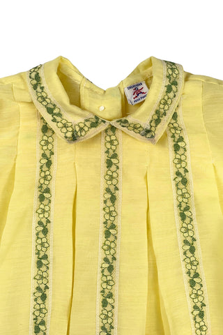 Vintage 1960s baby blouse top in sunshine yellow with accents of green and white lace. The top has three wide box pleats across the chest, with a small pointed collar, and short puffed sleeves. The top has a button closure down the back.

Designed by Creations Petit Poucet.