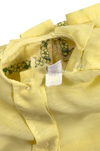 Vintage 1960s baby blouse top in sunshine yellow with accents of green and white lace. The top has three wide box pleats across the chest, with a small pointed collar, and short puffed sleeves. The top has a button closure down the back.

Designed by Creations Petit Poucet.