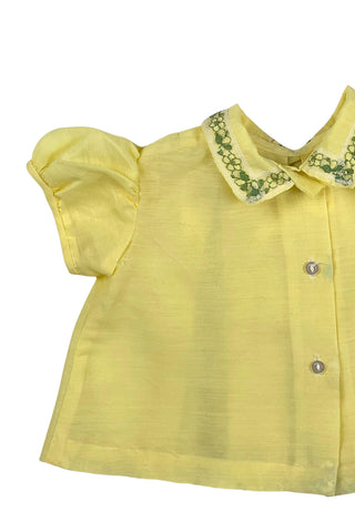 Vintage 1960s baby blouse top in sunshine yellow with accents of green and white lace. The top has three wide box pleats across the chest, with a small pointed collar, and short puffed sleeves. The top has a button closure down the back.

Designed by Creations Petit Poucet.