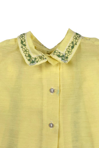 Vintage 1960s baby blouse top in sunshine yellow with accents of green and white lace. The top has three wide box pleats across the chest, with a small pointed collar, and short puffed sleeves. The top has a button closure down the back.

Designed by Creations Petit Poucet.