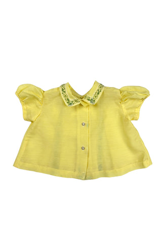 Vintage 1960s baby blouse top in sunshine yellow with accents of green and white lace. The top has three wide box pleats across the chest, with a small pointed collar, and short puffed sleeves. The top has a button closure down the back.

Designed by Creations Petit Poucet.