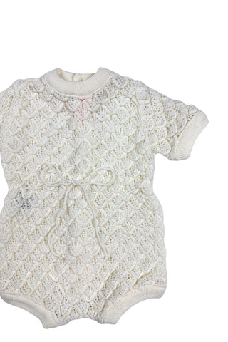 Vintage 1960s baby onesie bodysuit of cream crochet knit in a textural layered petal stitch. This beautiful and special piece would be perfect for baby’s layette.

Features a cord tie at the waist, which ties in a bow. The onesie closes in the back with five buttons up the back, and also has snap closures at the bottom.

Designed by Renzo. Made in Italy.
