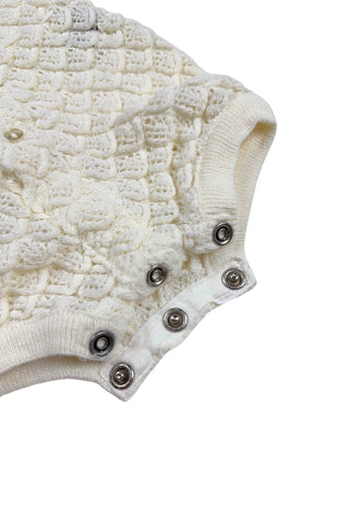 Vintage 1960s baby onesie bodysuit of cream crochet knit in a textural layered petal stitch. This beautiful and special piece would be perfect for baby’s layette.

Features a cord tie at the waist, which ties in a bow. The onesie closes in the back with five buttons up the back, and also has snap closures at the bottom.

Designed by Renzo. Made in Italy.