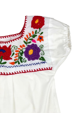 Vintage girls’ embroidered Mexican blouse with bright red, purple, pink, and orange flowers and green vines , featuring puffed sleeves with elasticized cuffs. The back of the shirt has a tiny purple flower.

The neckline and yoke are finished with a red blanket stitch.

The material feels like a cotton/poly blend.