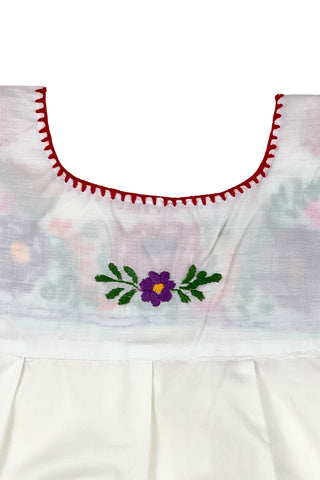 Vintage girls’ embroidered Mexican blouse with bright red, purple, pink, and orange flowers and green vines , featuring puffed sleeves with elasticized cuffs. The back of the shirt has a tiny purple flower.

The neckline and yoke are finished with a red blanket stitch.

The material feels like a cotton/poly blend.