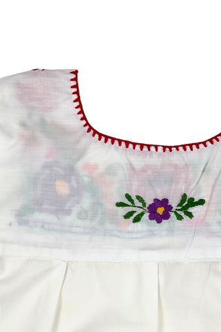 Vintage girls’ embroidered Mexican blouse with bright red, purple, pink, and orange flowers and green vines , featuring puffed sleeves with elasticized cuffs. The back of the shirt has a tiny purple flower.

The neckline and yoke are finished with a red blanket stitch.

The material feels like a cotton/poly blend.