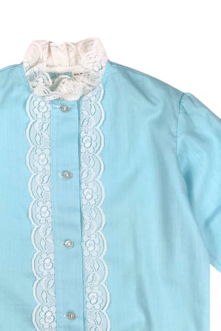 Vintage 1960s toddler blouse in blue cotton/poly blend with wide white lace down the button placket, and at the collar, cuffs, and hem.

Closes in the front with four ivory coloured buttons.