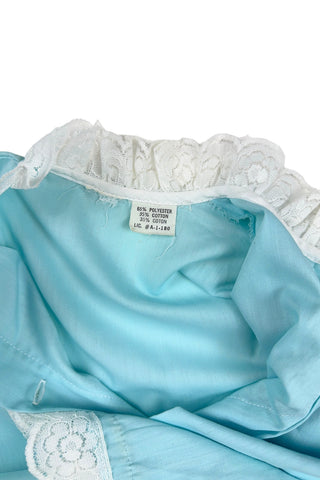 Vintage 1960s toddler blouse in blue cotton/poly blend with wide white lace down the button placket, and at the collar, cuffs, and hem.

Closes in the front with four ivory coloured buttons.