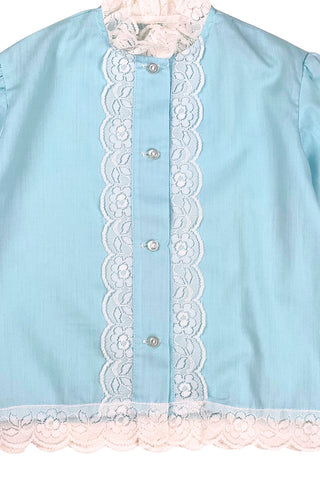 Vintage 1960s toddler blouse in blue cotton/poly blend with wide white lace down the button placket, and at the collar, cuffs, and hem.

Closes in the front with four ivory coloured buttons.