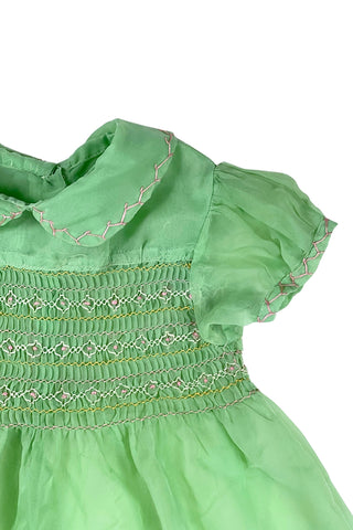 Vintage 1950s smocked baby dress in sheer light green gauze, with pink and white smocking stitching. The dress features a Peter Pan collar, puffed sleeves, and closes in the back with four lucite pink sparkle buttons. The collar and sleeves are trimmed with pink zigzag stitch.

The dress is in good vintage condition, with some areas where the seem has separated, which could be easily fixed.