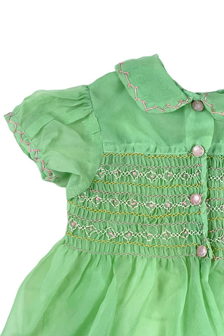 Vintage 1950s smocked baby dress in sheer light green gauze, with pink and white smocking stitching. The dress features a Peter Pan collar, puffed sleeves, and closes in the back with four lucite pink sparkle buttons. The collar and sleeves are trimmed with pink zigzag stitch.

The dress is in good vintage condition, with some areas where the seem has separated, which could be easily fixed.