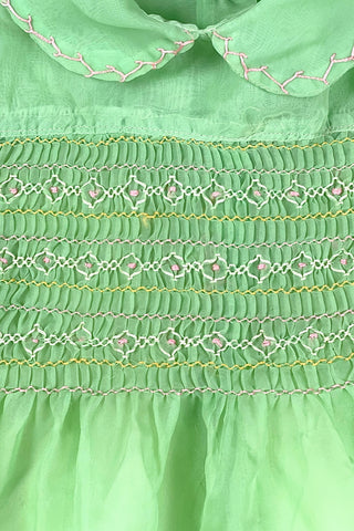 Vintage 1950s smocked baby dress in sheer light green gauze, with pink and white smocking stitching. The dress features a Peter Pan collar, puffed sleeves, and closes in the back with four lucite pink sparkle buttons. The collar and sleeves are trimmed with pink zigzag stitch.

The dress is in good vintage condition, with some areas where the seem has separated, which could be easily fixed.