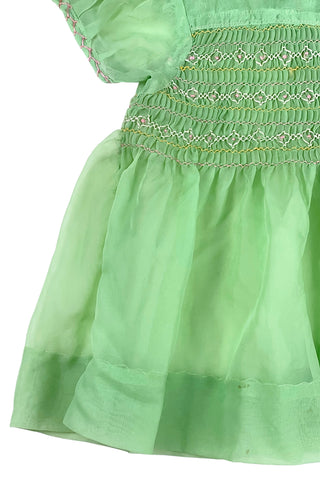 Vintage 1950s smocked baby dress in sheer light green gauze, with pink and white smocking stitching. The dress features a Peter Pan collar, puffed sleeves, and closes in the back with four lucite pink sparkle buttons. The collar and sleeves are trimmed with pink zigzag stitch.

The dress is in good vintage condition, with some areas where the seem has separated, which could be easily fixed.