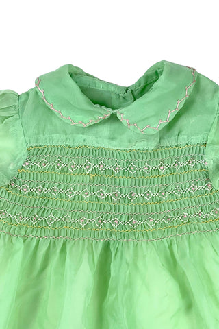 Vintage 1950s smocked baby dress in sheer light green gauze, with pink and white smocking stitching. The dress features a Peter Pan collar, puffed sleeves, and closes in the back with four lucite pink sparkle buttons. The collar and sleeves are trimmed with pink zigzag stitch.

The dress is in good vintage condition, with some areas where the seem has separated, which could be easily fixed.