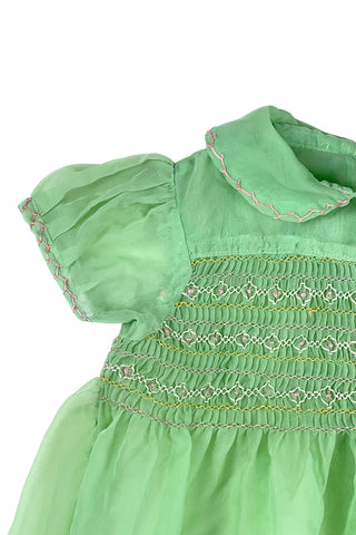 Vintage 1950s smocked baby dress in sheer light green gauze, with pink and white smocking stitching. The dress features a Peter Pan collar, puffed sleeves, and closes in the back with four lucite pink sparkle buttons. The collar and sleeves are trimmed with pink zigzag stitch.

The dress is in good vintage condition, with some areas where the seem has separated, which could be easily fixed.