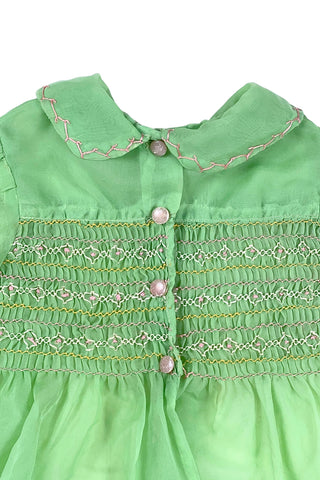 Vintage 1950s smocked baby dress in sheer light green gauze, with pink and white smocking stitching. The dress features a Peter Pan collar, puffed sleeves, and closes in the back with four lucite pink sparkle buttons. The collar and sleeves are trimmed with pink zigzag stitch.

The dress is in good vintage condition, with some areas where the seem has separated, which could be easily fixed.