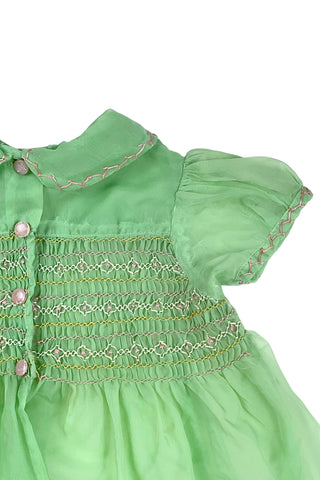 Vintage 1950s smocked baby dress in sheer light green gauze, with pink and white smocking stitching. The dress features a Peter Pan collar, puffed sleeves, and closes in the back with four lucite pink sparkle buttons. The collar and sleeves are trimmed with pink zigzag stitch.

The dress is in good vintage condition, with some areas where the seem has separated, which could be easily fixed.