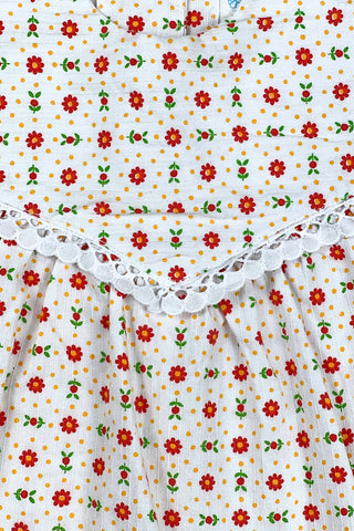 Vintage 1960s toddler girls’ white sleeveless dress featuring a red, yellow, and green floral pattern with white eyelet lace trim.

Made in Austria.