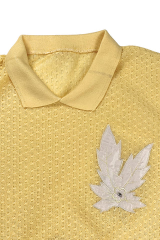 Vintage 1980s short sleeve sweater with ribbed collar and cuffs in sunny yellow tiny eyelet knit with a white leaf appliqué accented with a rhinestone center.