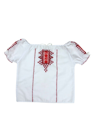 Vintage 1970s peasant blouse in white cotton with red hand embroidery stitching and red and white floral appliqué embroidered patches on the chest and sleeves. The neckline and sleeves are gathered with tiny white cord drawstring. The edges of the sleeves are trimmed with red blanket stitch.