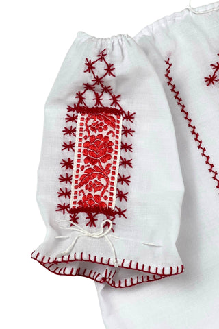 Vintage 1970s peasant blouse in white cotton with red hand embroidery stitching and red and white floral appliqué embroidered patches on the chest and sleeves. The neckline and sleeves are gathered with tiny white cord drawstring. The edges of the sleeves are trimmed with red blanket stitch.