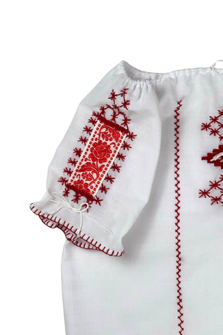Vintage 1970s peasant blouse in white cotton with red hand embroidery stitching and red and white floral appliqué embroidered patches on the chest and sleeves. The neckline and sleeves are gathered with tiny white cord drawstring. The edges of the sleeves are trimmed with red blanket stitch.