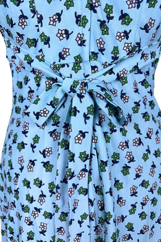 Vintage 1960s mini dress in sky blue with green and white floral print. The V neck and short sleeves are trimmed with wide white lace ruffles. The dress has an inset waistband, with slightly gathered bust. The A-line skirt hits at mid-thigh. The dress closes in the back with a cotton twill zipper and bow sash tie, and is unlined.